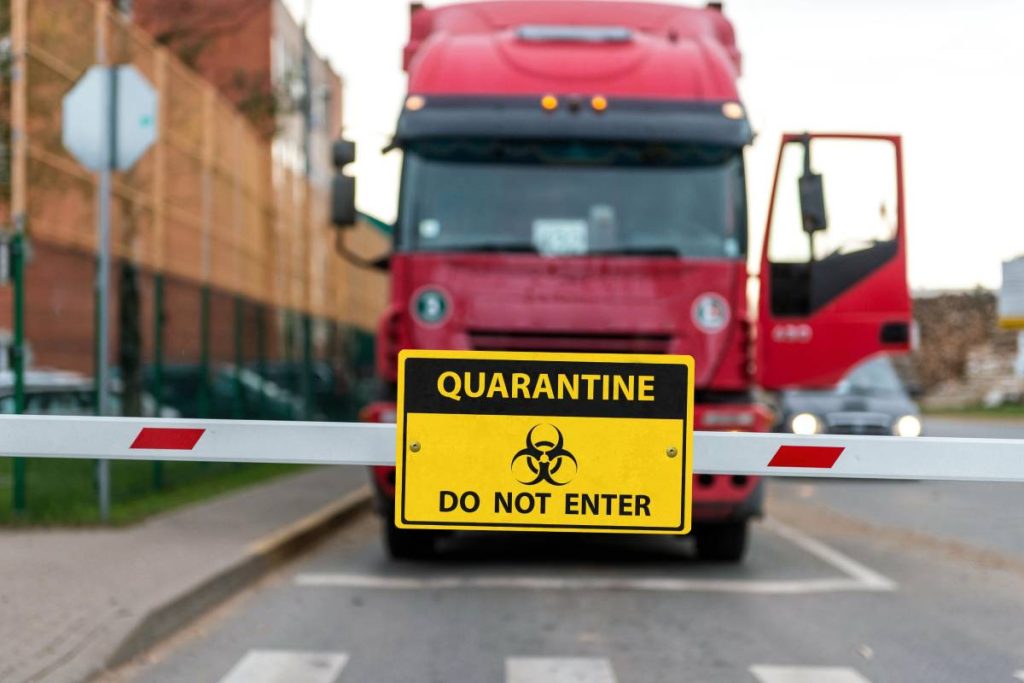 Truck standing at the barrier with a virus warning sign, Coronavirus containment concept