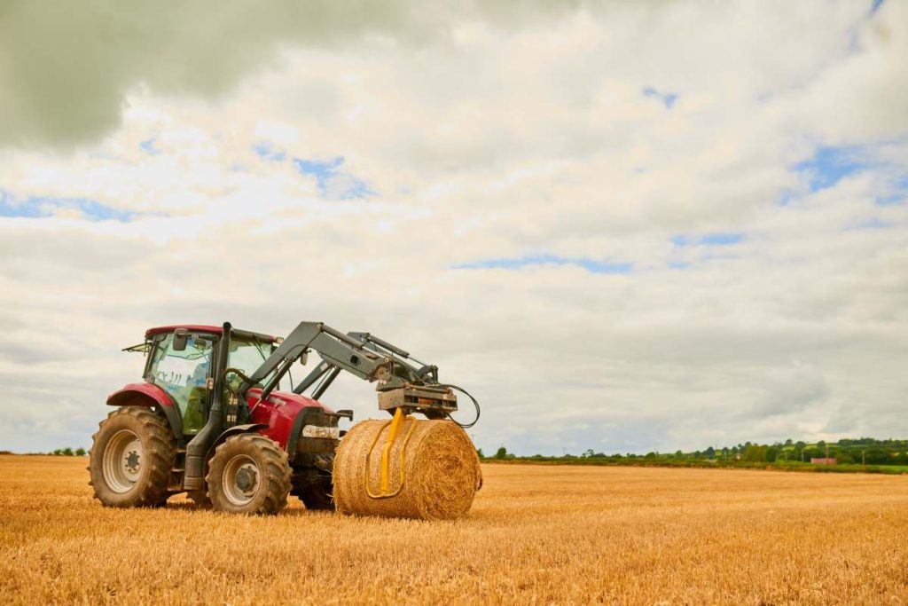 His farm is well-kept. Shot of a farmer stacking hale bales with a tractor on his farm