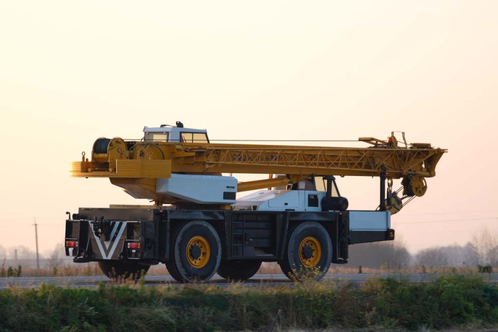 Heavy duty mobile lifting crane driving on intercity road at sunset.