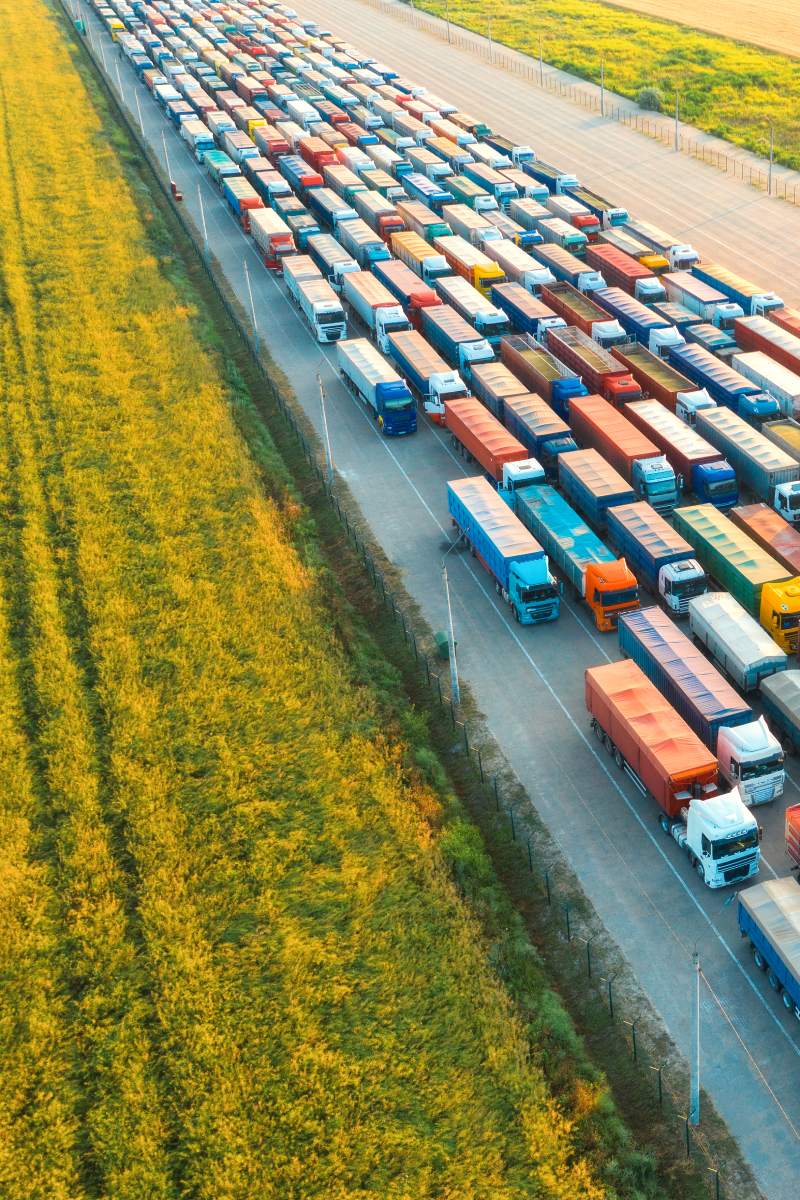 Aerial view of colorful trucks in terminal at sunset in summer. Top view of logistic center. Heavy industry. Transportation. Cargo transport, shipping. International trucking. View from drone of truck