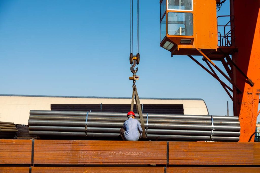 Worker preparing stack of metal pipes for transporting with gantry crane in the steel factory