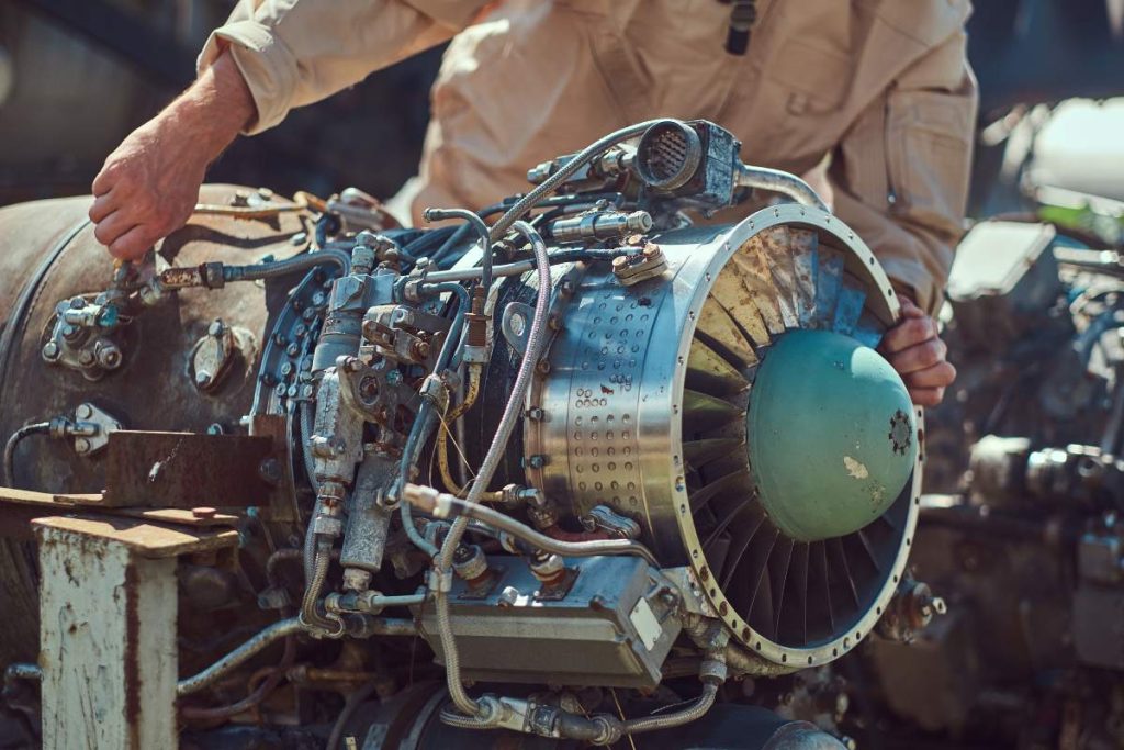 Portrait of a pilot-mechanic in uniform and flying helmet, repairing the dismantled airplane turbine in an open-air museum.