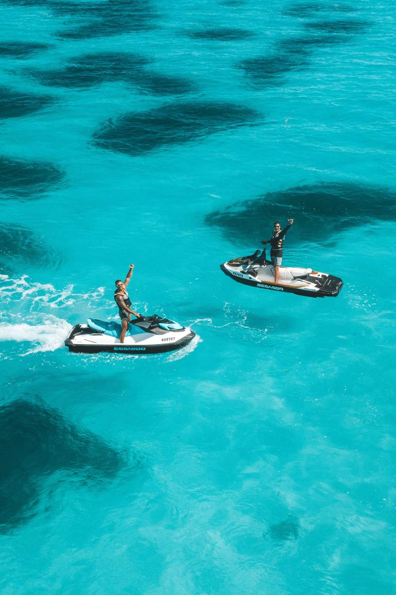 Two people riding jet skis on clear blue water, enjoying a sunny day